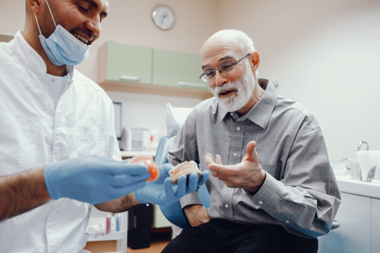 Handsome old man talking to the dendist. Two men in the dentist's office. The doctor shows the patient dentures